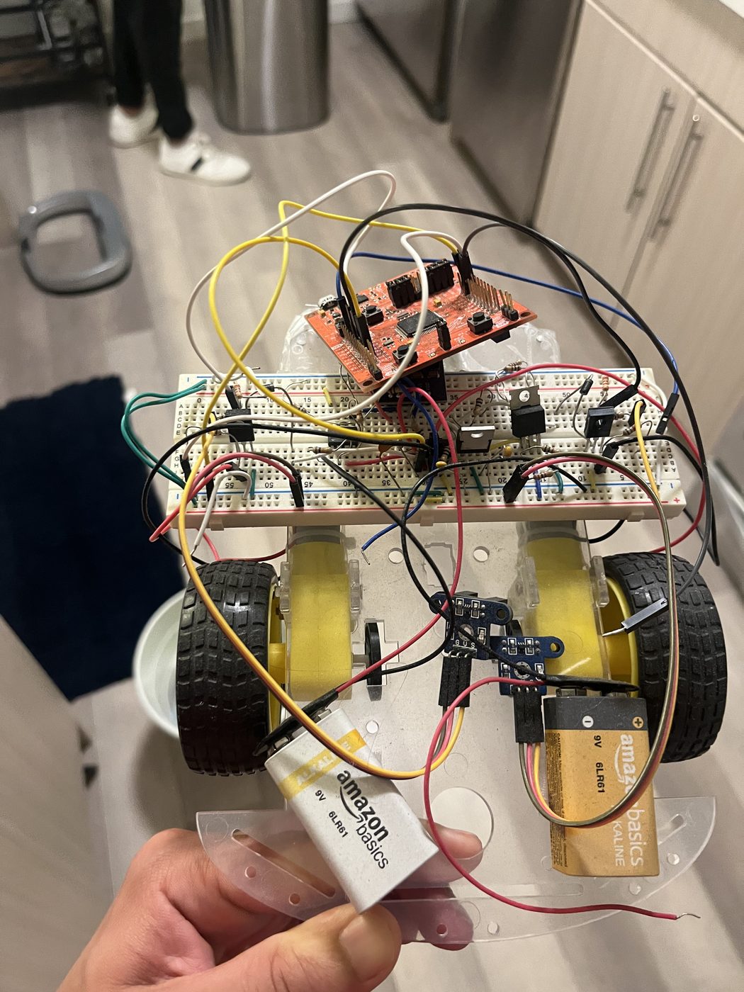 Hand holding a homemade robot car with wires and a breadboard