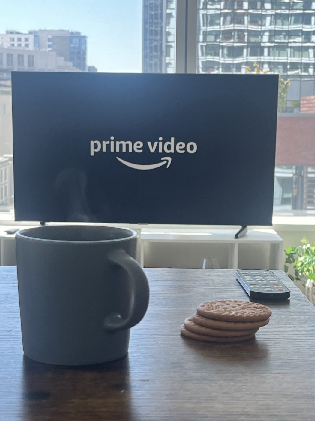 Mug and biscuits on a table in front of a TV and city windows